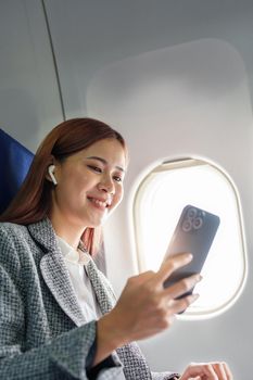 A successful asian businesswoman or female entrepreneur in formal suit in a plane sits in a business class's seat and uses a smartphone during flight.