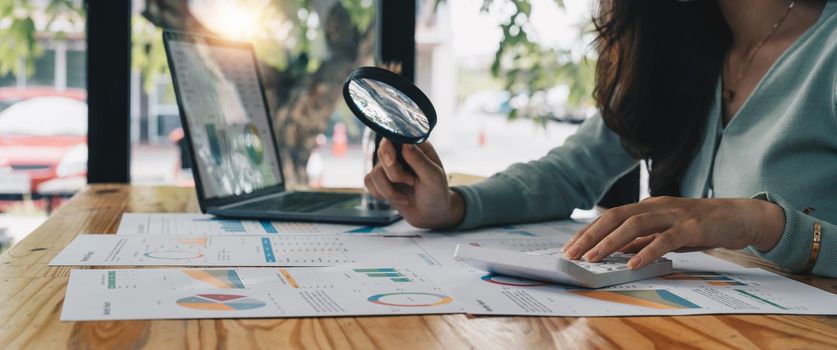 Tax inspector and financial auditor looking through magnifying glass, inspecting company financial papers, documents and reports.