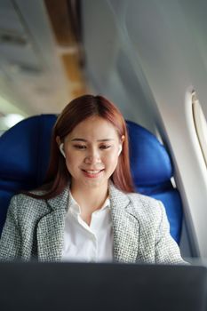 portrait of A successful asian businesswoman or female entrepreneur in formal suit in a plane sits in a business class seat and uses a computer laptop during flight.
