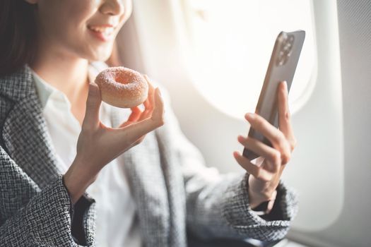 portrait of A successful asian businesswoman or female entrepreneur in formal suit in a plane sits in a business class seat and eating and using smartphone during flight.