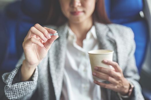 a successful Asian businesswoman or entrepreneur in a formal suit on an airplane in business class taking motion sickness pills during the flight.