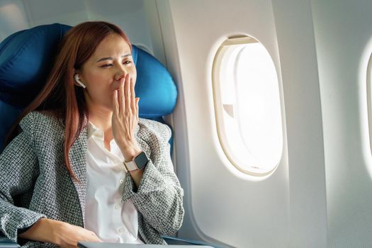 Portrait of a successful Asian businesswoman or entrepreneur in a formal suit on an airplane in business class waking up from resting between flights.