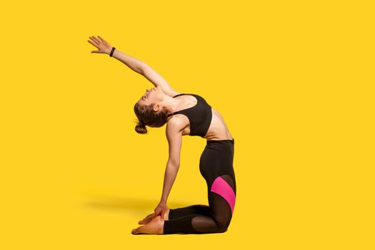 Camel pose. Athletic woman with hair bun in tight sportswear practicing yoga, doing spinal back bending ustrasana exercise with raised hand, stretching muscles. full length studio shot, sport workouts