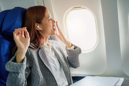 Portrait of a successful Asian businesswoman or entrepreneur in a formal suit on an airplane in business class waking up from resting between flights.