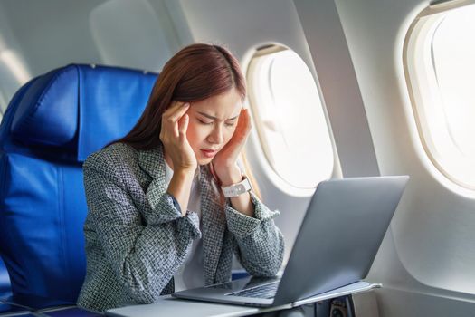 portrait of a successful Asian businesswoman or entrepreneur in a formal suit on an airplane seated in Business Class shows a thoughtful and stressed face with using laptop during the flight.