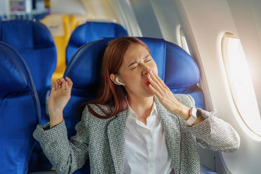 Portrait of a successful Asian businesswoman or entrepreneur in a formal suit on an airplane in business class waking up from resting between flights.