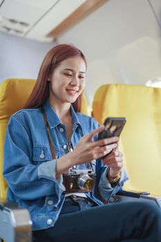 Attractive portrait of Asian woman sitting at window seat in economy class using mobile phone during plane flight, travel concept, vacation.