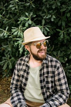 Laughing attractive man wearing hat over green tree background - emotion and vacation travel holidays