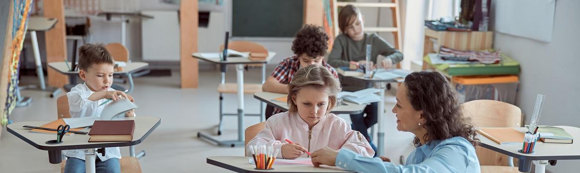 Happy kind teacher is helping kids in elementary school lessons.