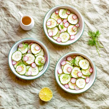 three small round bowls with radish and cucumber summer light salad, green textile background, top view