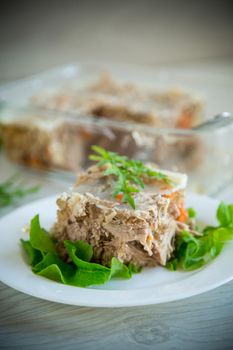 jellied meat with greens and vegetables in a plate on a wooden table