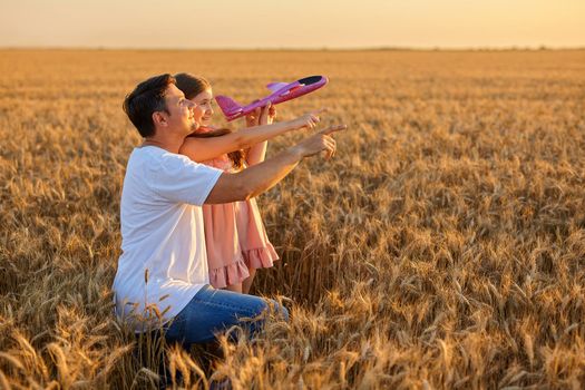 Cute girl and her father playing with toy airplane against sky in wheat field