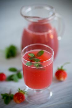 Cold summer strawberry kvass with mint in a glass on a wooden light table