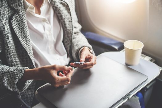 a successful Asian businesswoman or entrepreneur in a formal suit on an airplane in business class taking motion sickness pills during the flight.