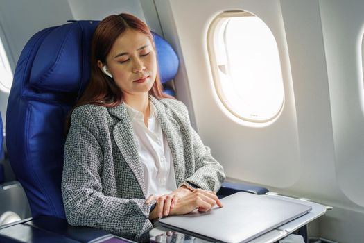 portrait of Successful Asian businesswoman or entrepreneur in a formal suit on an airplane seated in business class. resting during the flight.