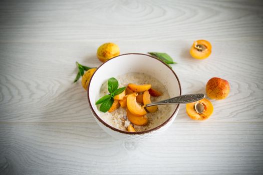 Healthy breakfast of boiled oatmeal with fresh apricots in a bowl on the table.