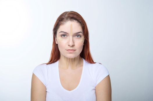 Portrait of a redhead woman with tapes on skin color face for rejuvenation. An alternative way to fight wrinkles