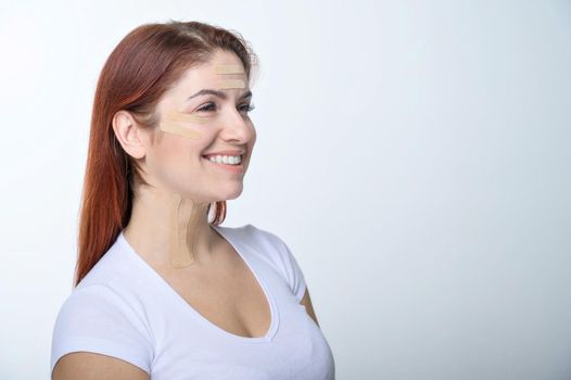 Portrait of a redhead woman with tapes on skin color face for rejuvenation. An alternative way to fight wrinkles