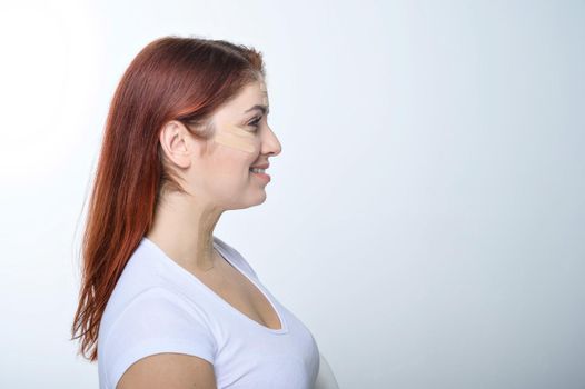 Profile red-haired woman with tape on the skin complexion rejuvenation. An alternative way to fight wrinkles