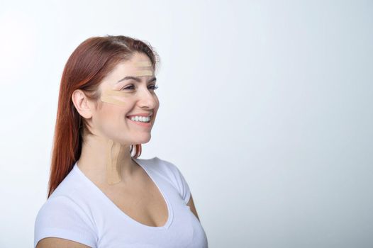 Portrait of a redhead woman with tapes on skin color face for rejuvenation. An alternative way to fight wrinkles