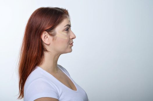 Profile red-haired woman with tape on the skin complexion rejuvenation. An alternative way to fight wrinkles