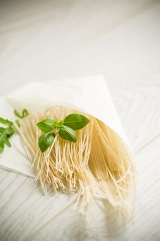 homemade thin dried egg noodles in a paper bag with basil, on a wooden table