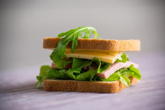 sandwich with various greens, cheese, sausage, tomato on a wooden table