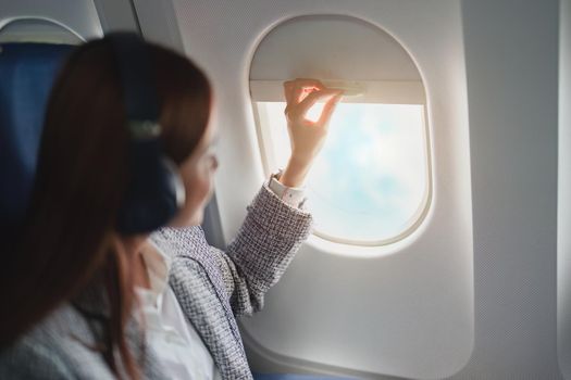 A successful Asian businesswoman or entrepreneur in a formal suit on an airplane sits in business class, looking through the window in the during the flight and listening to music.