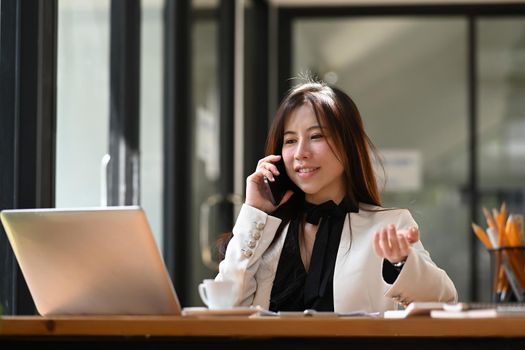 Attractive business woman talking on smart phone and working with laptop computer.