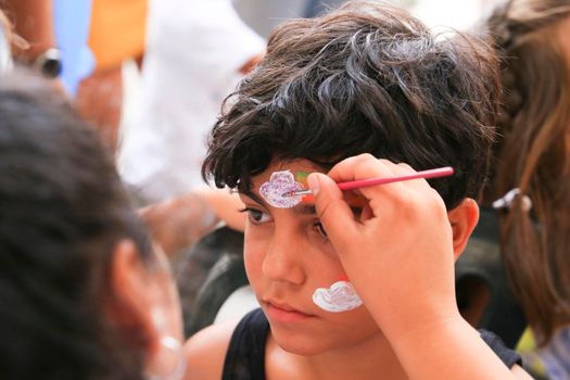 Alicante, Spain- July 2, 2022: Little boy with dark hair at face painting stall in Spain