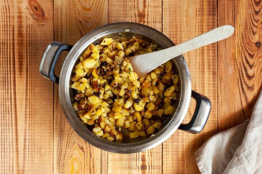 fried potatoes in a pan on the wooden background, top view