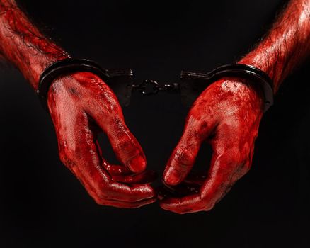 Close-up of male bloody handcuffed hands on a black background