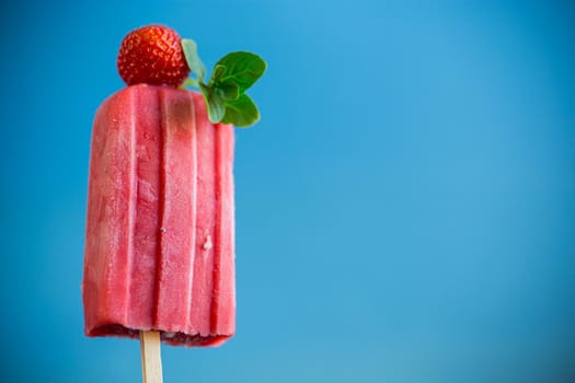 cooked homemade strawberry ice cream on a stick, isolated on blue background