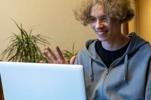 A young guy is chatting in a video chat via a laptop. video call. Remote communication. A happy Caucasian guy waves his hand at the laptop camera. Video call via computer, Communication with family