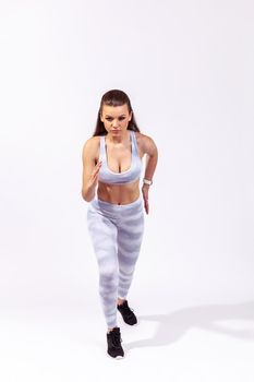 Full length active persistent woman in white sportswear ready to run, standing on start position, sprint. Indoor studio shot isolated on gray background