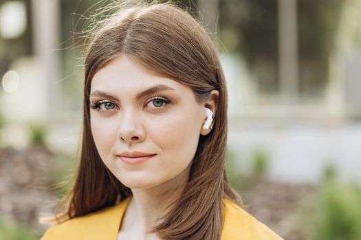 Face of pretty young girl in wireless earphones outside. Woman with wireless earphones on her ears.