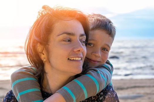 Cute happy preschooler boy hugs his mom on the seashore in the sunset light. love for parents. Close family relationships