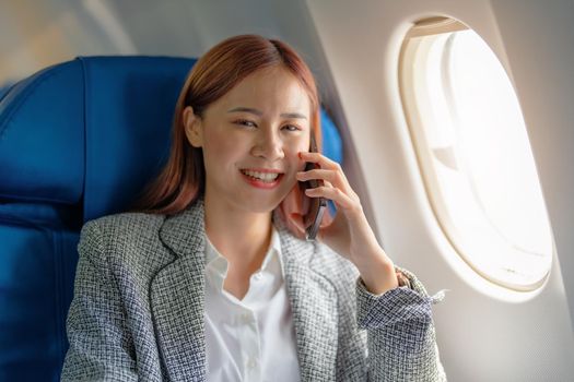 A successful asian businesswoman or female entrepreneur in formal suit in a plane sits in a business class's seat and uses a smartphone during flight.