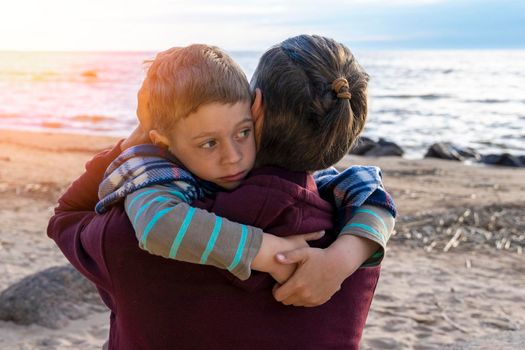 Cute sad preschool boy hugs his dad on the seashore in the sunset light. love for parents. Close family relationships