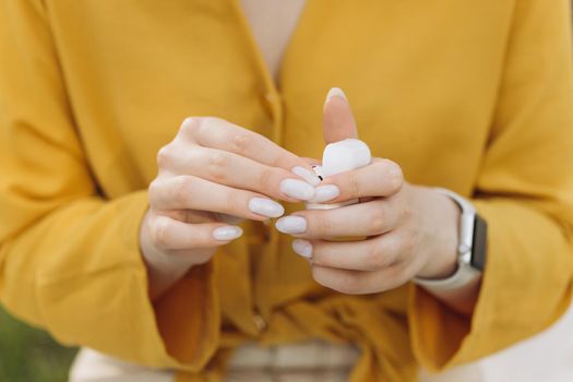 Closeup of woman taking out a white wireless earbuds from his charging box. Female hands touching a portable gadget headphones.