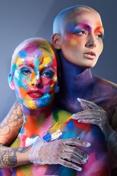 Studio shot of two young women posing with multi-coloured paint on her face.