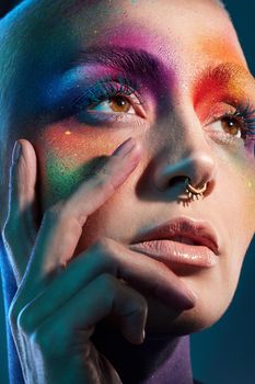 Studio shot of a young woman posing with multi-coloured paint on her face.