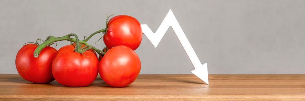 The price of tomatoes and vegetables. Bad vegetable harvest. Fresh red ripe tomatoes with twigs on the table. Graph chart points down