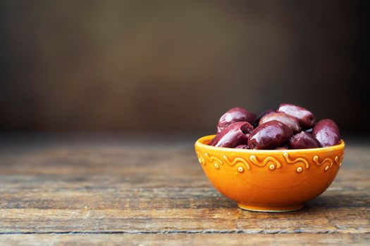 Greek ceramic bowl full of pitted kalamata olives on rustic wooden table with copy space.