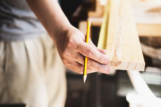 A carpenter measures the planks to assemble the parts and build a wooden table for the customer