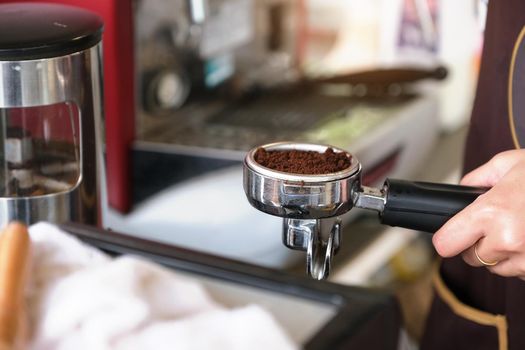 A female worker presses the finely ground coffee beans against a tamper.