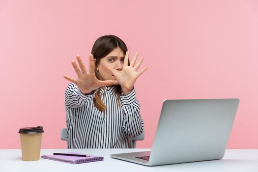 No, I'm scared. Frightened woman with shocked expression raising hands in stop gesture, defending herself, freaked out of troubles working on laptop. Indoor studio shot isolated on pink background