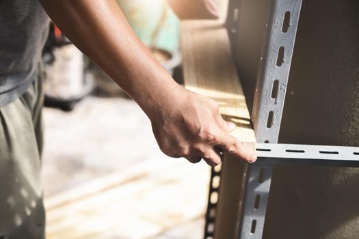 A craftsman puts a wooden board on a steel shelf he has assembled in his spare time.