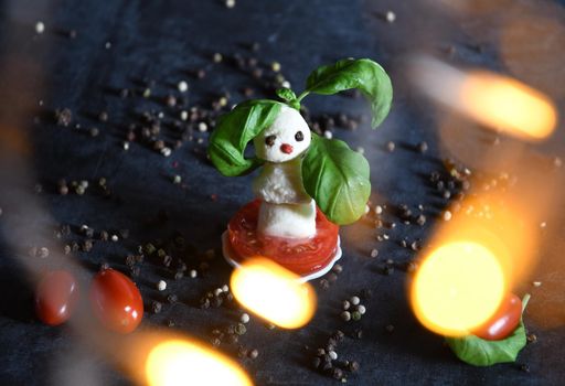 creative snowman canapes of mozzarella and tomatoes on a background of red poinsettia and a scattering of black pepper and green basil. High quality photo