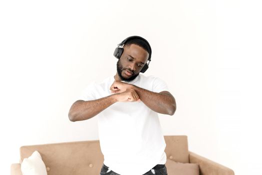 African American man enjoying music in wireless big headphones and dancing at home. Relax alone.
